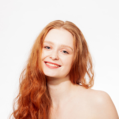 Close-up studio portrait of a young attractive cheerful red-haired woman against a white background