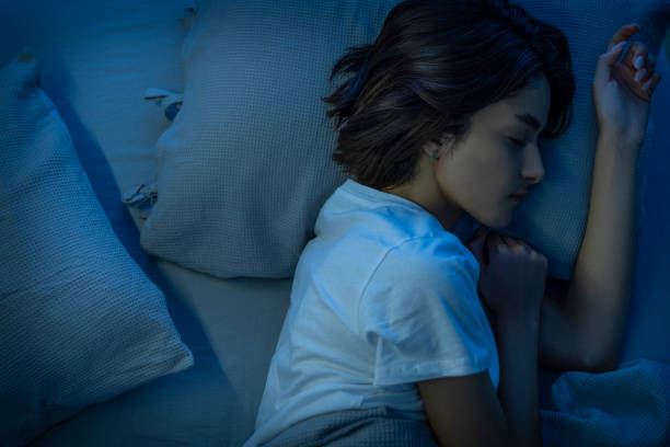 Woman sleeping cozily on a bed in her bedroom at night