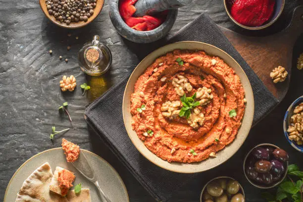 Arabic Cuisine: Middle Eastern delicious dip "Muhammara". It is a hearty walnut and roasted red pepper dip. Served with fresh olives, olive oil and pita bread. Top view with copy space.