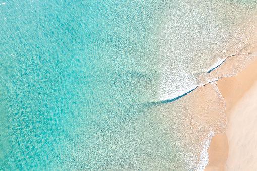 Drone view of an idyllic ocean with gentle waves near a stunning sand beach at a holiday resort