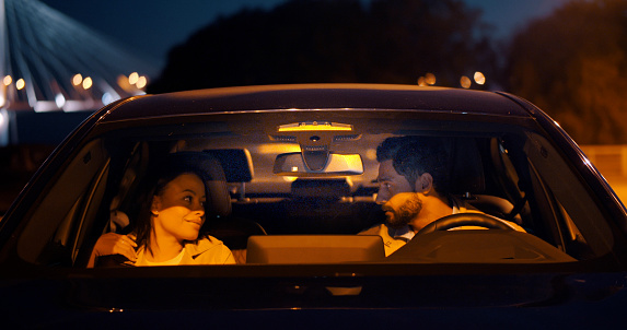 Diverse husband and wife together sitting in car on parking lot . Multiethnic couple sit in car and chat