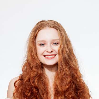 Close-up studio portrait of a young attractive cheerful red-haired woman against a white background