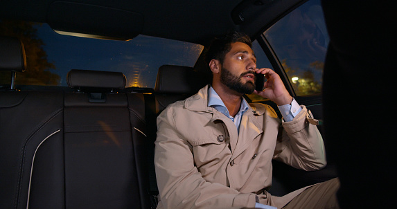 Young confident man talking over phone while sitting in taxi. Businessman sitting on backseat of car using mobile phone to communicate