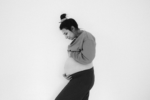 Portrait of a pregnant woman and her growing belly isolated on a white background; daydreaming about her future child.