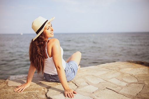 Beautiful girl with straw hat enjoying sunbath at beach. Close up face of young tanned woman Carefree latin woman smiling with ocean in background.