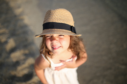Portrait of preschool girl with straw hat. Cute happy toddler child looking at the camera and smiling. Lovely girl on summer vacations with family
