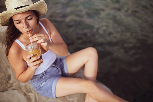 Beautiful girl with straw hat enjoying sunbath at beach. Close up face of young tanned woman Carefree latin woman smiling with ocean in background.