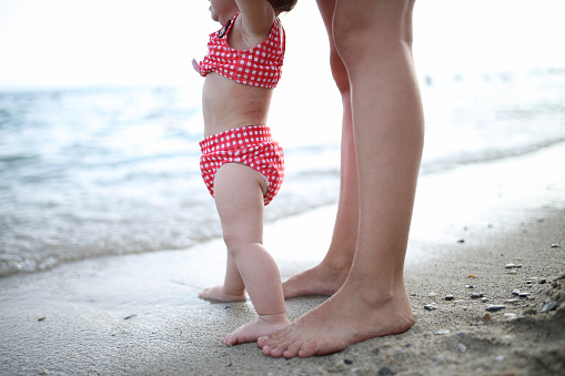 Baby walks on the sea beach and learns to walk with his mother. First steps, parental care and love concept. High quality photo