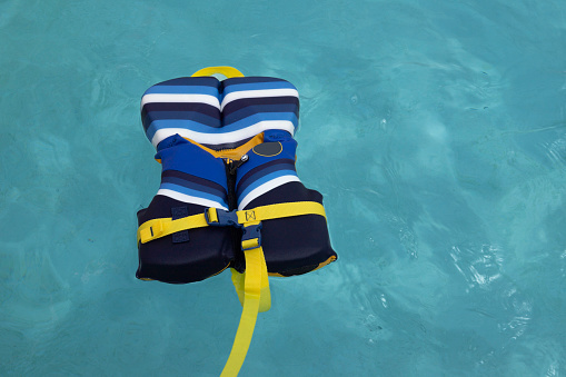 blue and yellow life preserver life vest floating in blue water with no people,  copy space, used to prevent drowning