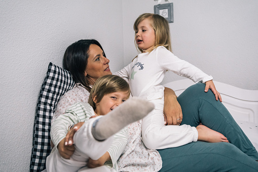 Mother of single parent family playing sitting in bed with her two blond children.