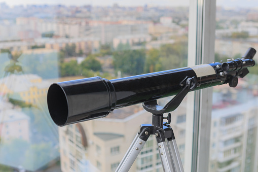 Telescope in the interior near the window against the backdrop of the city close-up
