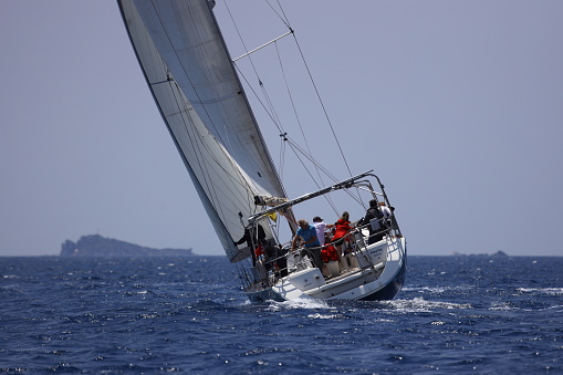 Bodrum,Mugla, Turkey. May 07, 2023: sailor team driving sail boat in motion, sailboat wheeling with water splashes, mountains and seascape on background. Sailboats sail in windy weather in the blue waters of the Aegean Sea, on the shores of the famous holiday destination Bodrum