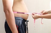 doctor measures waist circumference of pot-bellied man