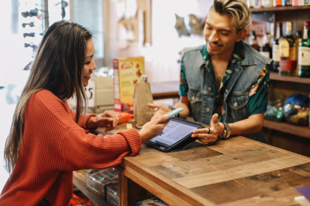 contactless payment at the convenience store Woman shopping for drinks and snacks in a small convenience store in Los Angeles, California, paying contactless with smartphone. liquor store counter photos stock pictures, royalty-free photos & images