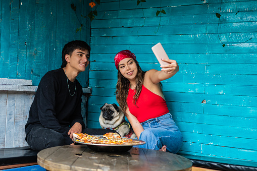 Young couple taking a selfie with a pizza and their dog