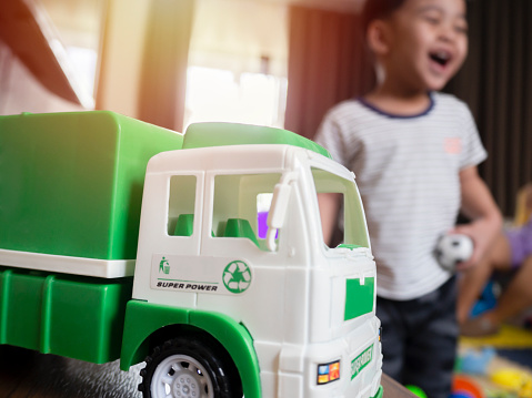 Close up of green truck toy and a blurred image of an Asian boy laughing happily in the background. Family happiness concept.