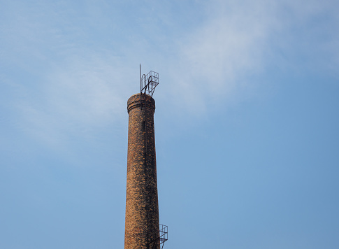 chimney of a waste-to-energy plant with metal ladder outside and antennas at platform