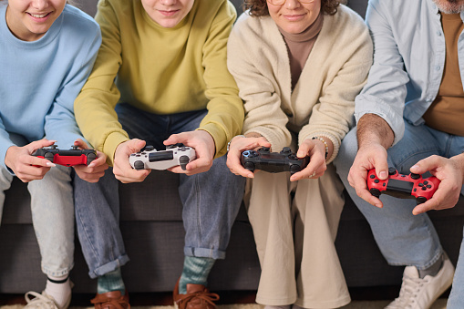 Close-up of family of four using joysticks to play game console together at home
