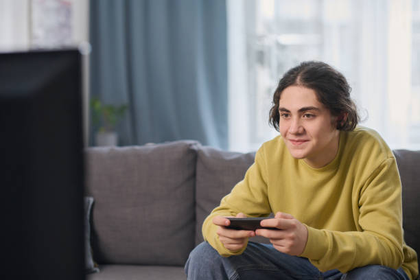 istock Teenage boy playing video game at home 1491638557