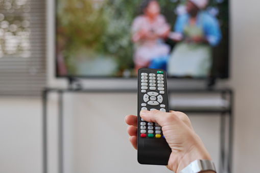 Close-up of woman switching channels on TV with remote control during her leisure time at home