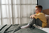 Side view of lonely sad little boy sitting on bed with hugging knee and sadness looking away, feeling pressure and problem. Thoughtful child resting alone