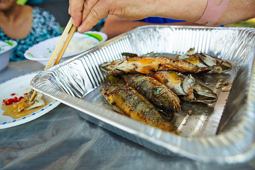 Senior Vietnamese senior eating deep-fried fish dipping with fish sauce at camping