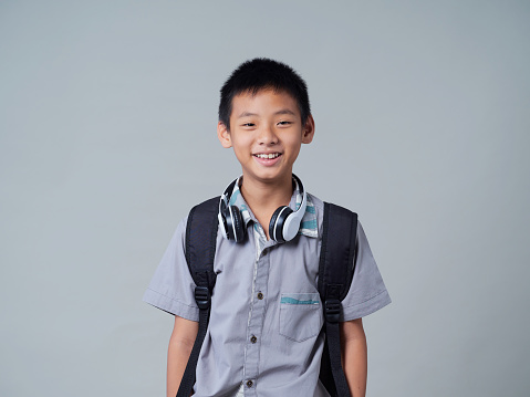 portrait of a boy with backpack wearing headphones grey background