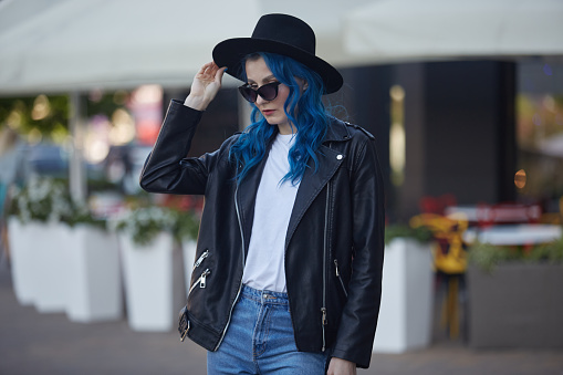 Beautiful female person in leather jacket and hipster hat standing outside a street cafe