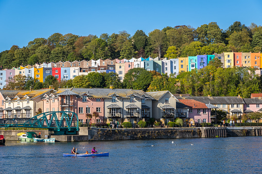 Bristol, UK - 8 October, 2022 - Rows of colourful terraced houses in Cliftonwood, overlooking Bristol Harbourside, where tourists are rowing a boat on Bristol Feeder Canal
