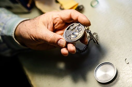 Hands of senior watch maker repairing an old pocket watch