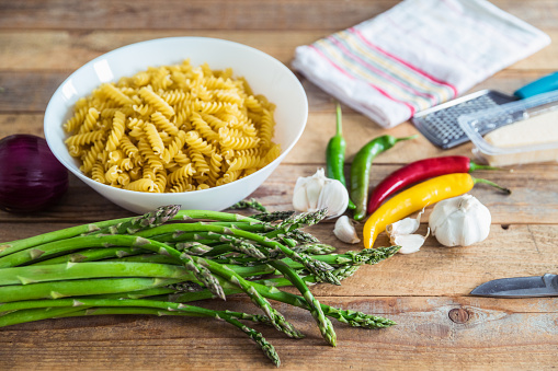Raw asparagus on table with fusilli pasta, chili, red onions and garlic on table, close up, selective focus
