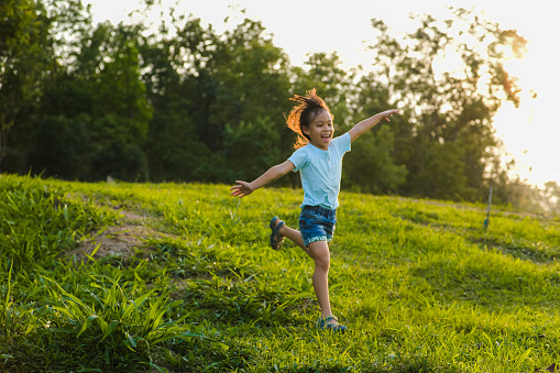 Happy little girl running on the grass in the summer park. Little girl running through the meadow with sunset light.