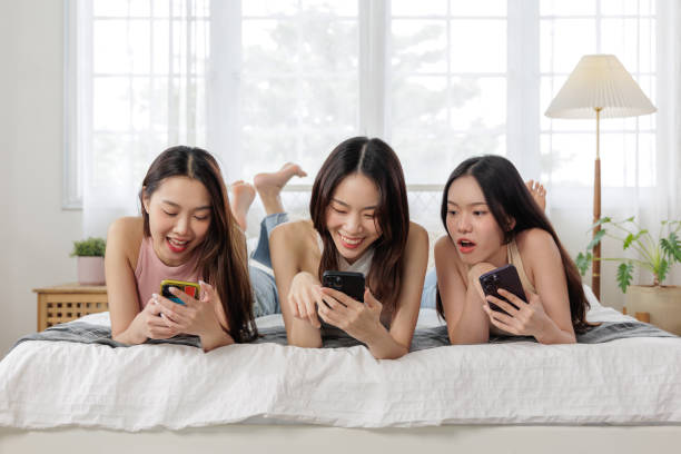 istock Asian women laughing while watching content on smartphones in bed 1491674992
