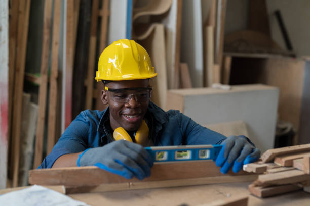istock Male carpenter using water level measure during working in wood workshop. Male joiner wearing safety uniform, gloves, helmet and working in furniture workshop 1491675861