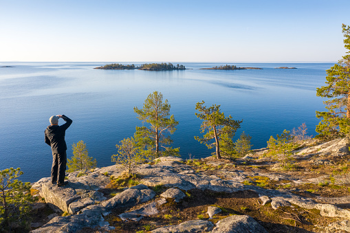 A man on a rocky island with pine trees looks into the sea.