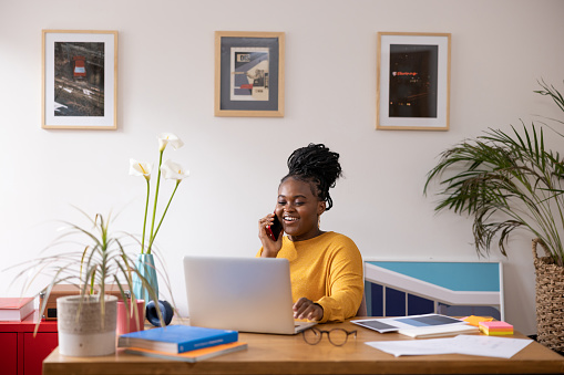 Black woman in her 20s working from her modern home office and talking on her cellphone