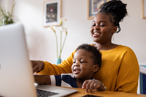 African American mother entertaining her son while working from her home office using her computer
