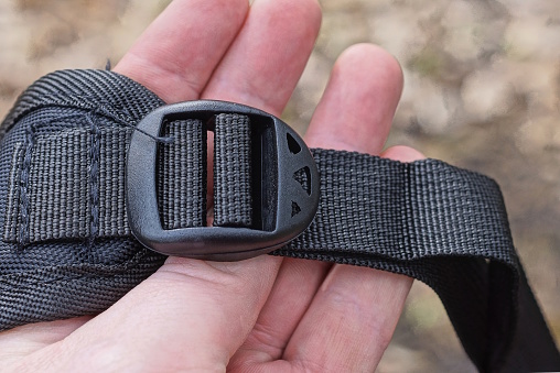 hand hold a one closed small black plastic carabiner on a harness in the backpack