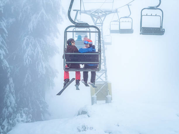 Young Multiracial Skiers Smiling on Ski Lift, Misty Day stock photo