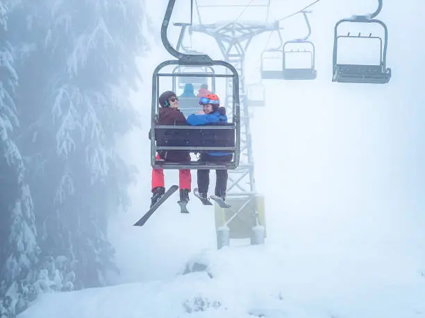 Photo of Young Multiracial Skiers Smiling on Ski Lift, Misty Day