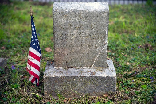 Civil war soldier grave with dated stone and green grass field. American flag is beside it