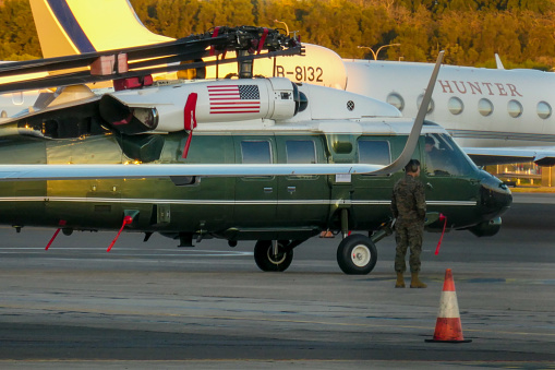 A helicopter used to transport the US President is prepared for loading into a Boeing C-17A Globemaster III, registration 06-6155.  In the background is a Gulfstream G550, registration B-8132.  In the foreground is the wing and wingtip of a Dassault Falcon 7X of the Royal Australian Air Force, registration A56-001.  This image was taken from Ross Smith Avenue at Sydney Kingsford-Smith Airport at sunset on a cold autumn day on 20 May 2023.