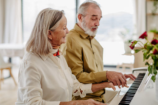 Senior couple playing on piano together in their livingroom.