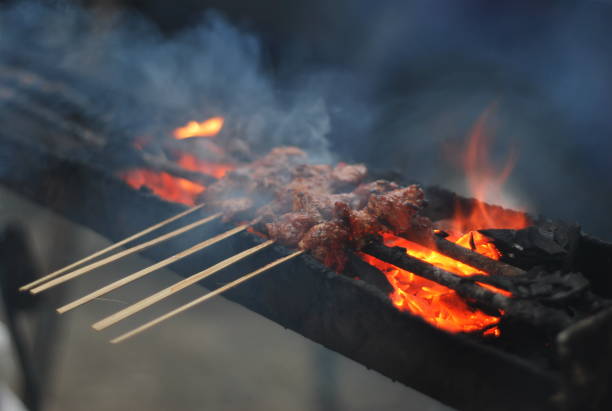 the satay is being grilled over charcoal.  This food is typical Indonesian food