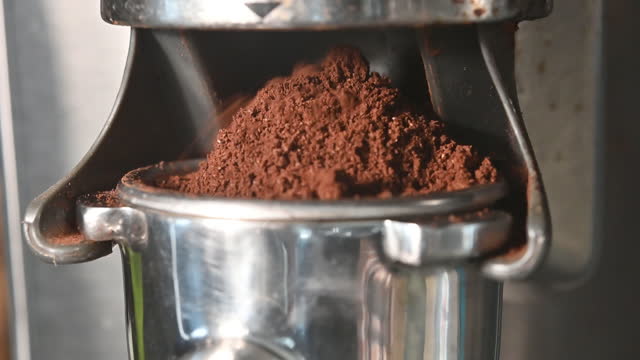 Freshly grounded coffee falling from grinding cradle into portafilter overflowing