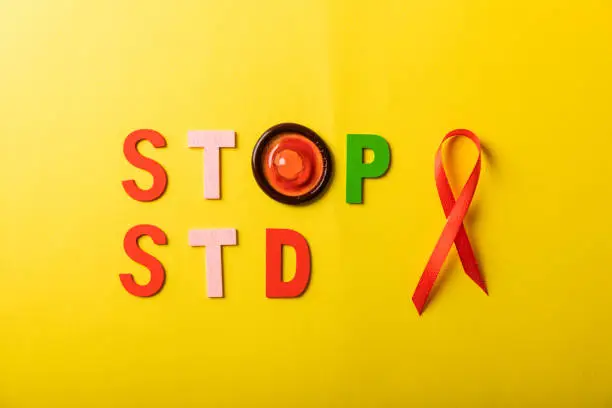 Colorful blocks with "STOP STD" phrase background, flat lay. Super safe strawberry condoms with a pleasant smell on a yellow background. Contraceptives are made from natural rubber latex, high