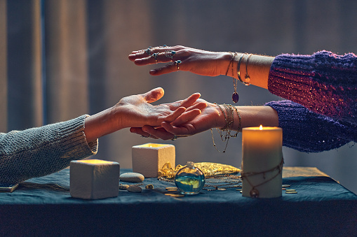 Witch woman spelling over hand palm during occult spiritual rite and divination ritual around candles and other magical accessories. Magic concept