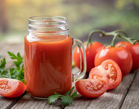 Glass of nutritious tomato juice with fresh tomatoes on rustic wooden table
