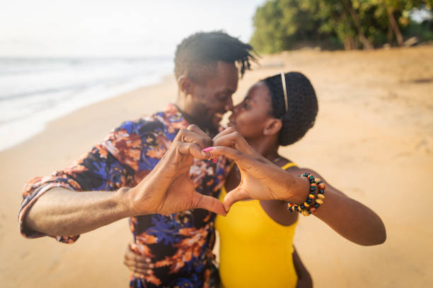 dos amantes en la playa hacen corazones con sus manos y tienen un momento apasionante - honeymoon beach couple heterosexual couple fotografías e imágenes de stock