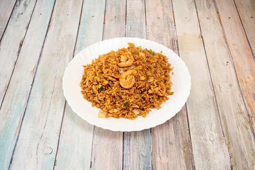 Fried rice with vegetables and prawns and drizzled with soy sauce cooked by the chef of a Chinese restaurant on white plate and wooden table